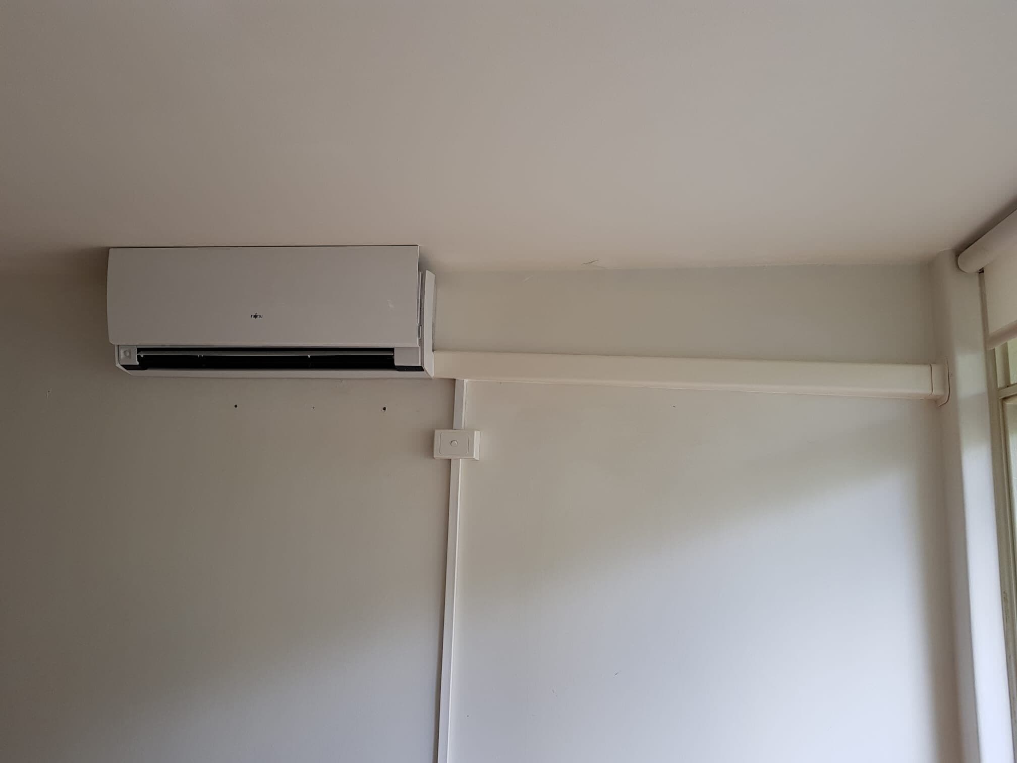 A wall-mounted split-system head in Albert Park with a clean white capping run carried across to the ceiling and a wall controller below