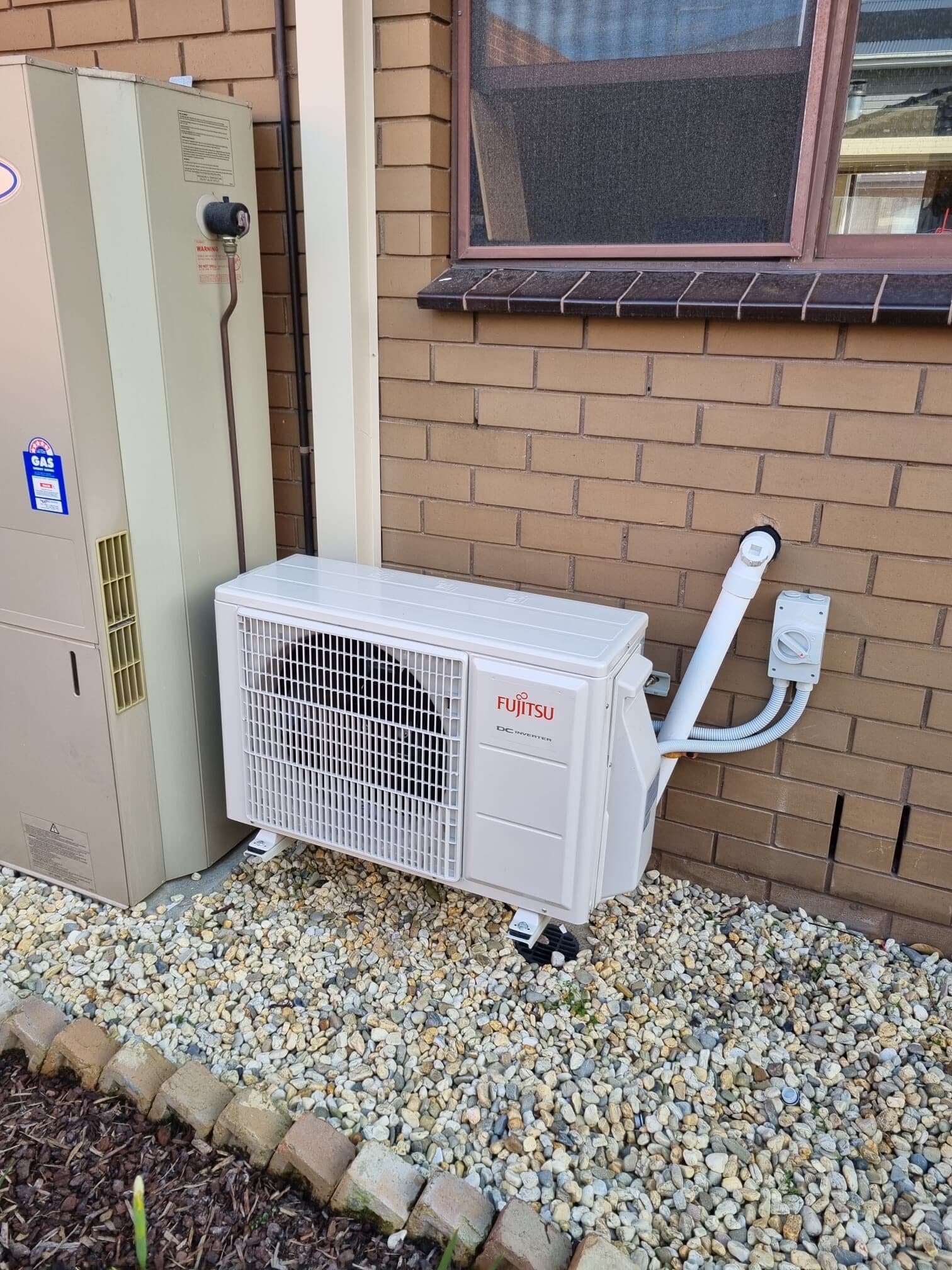 An outdoor condenser on wall brackets against a brick house wall in Brunswick with neatly lagged pipework