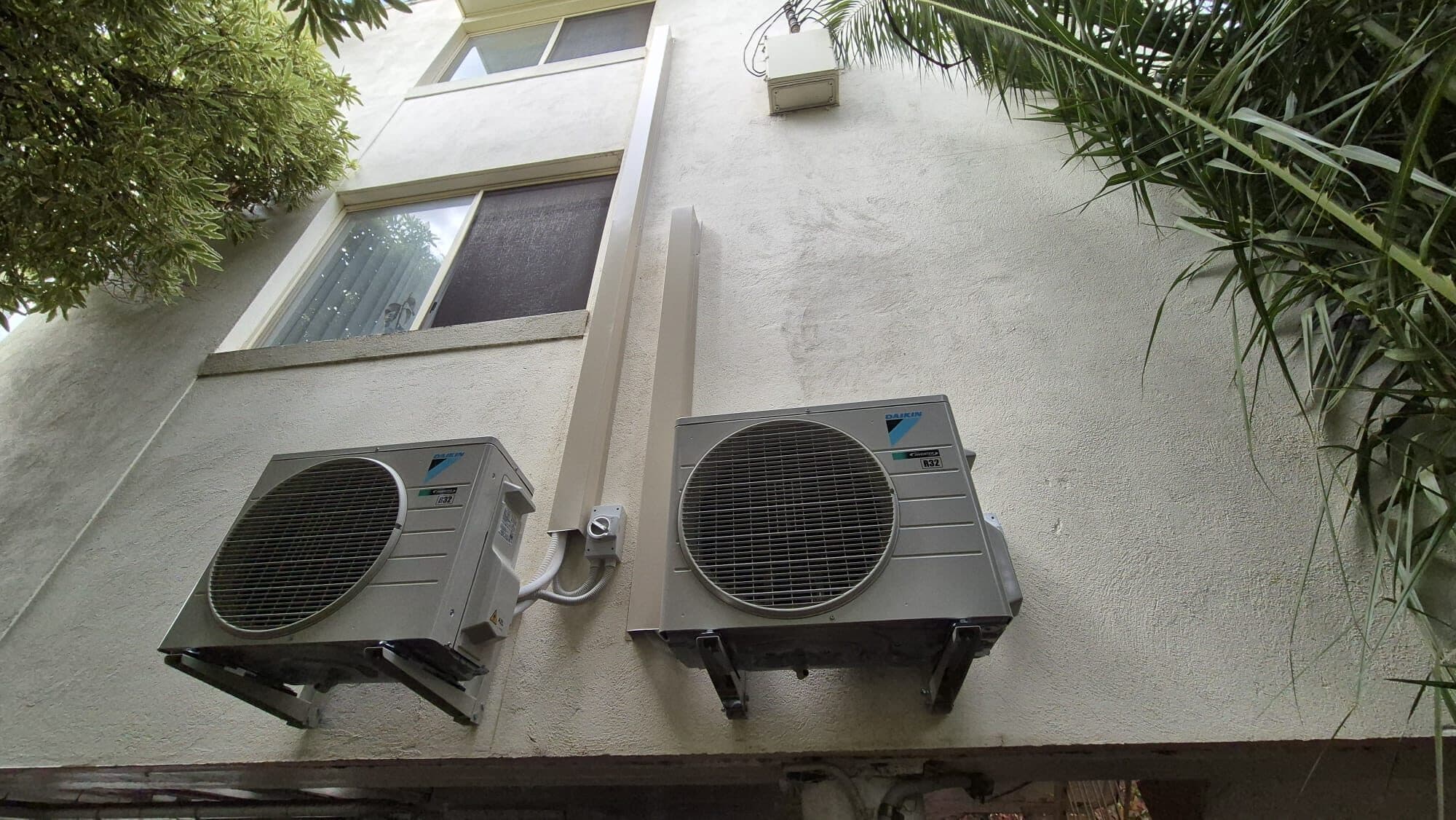 Two outdoor condensers bracket-mounted on a rendered apartment facade in Carlton with a tidy capping drop between them