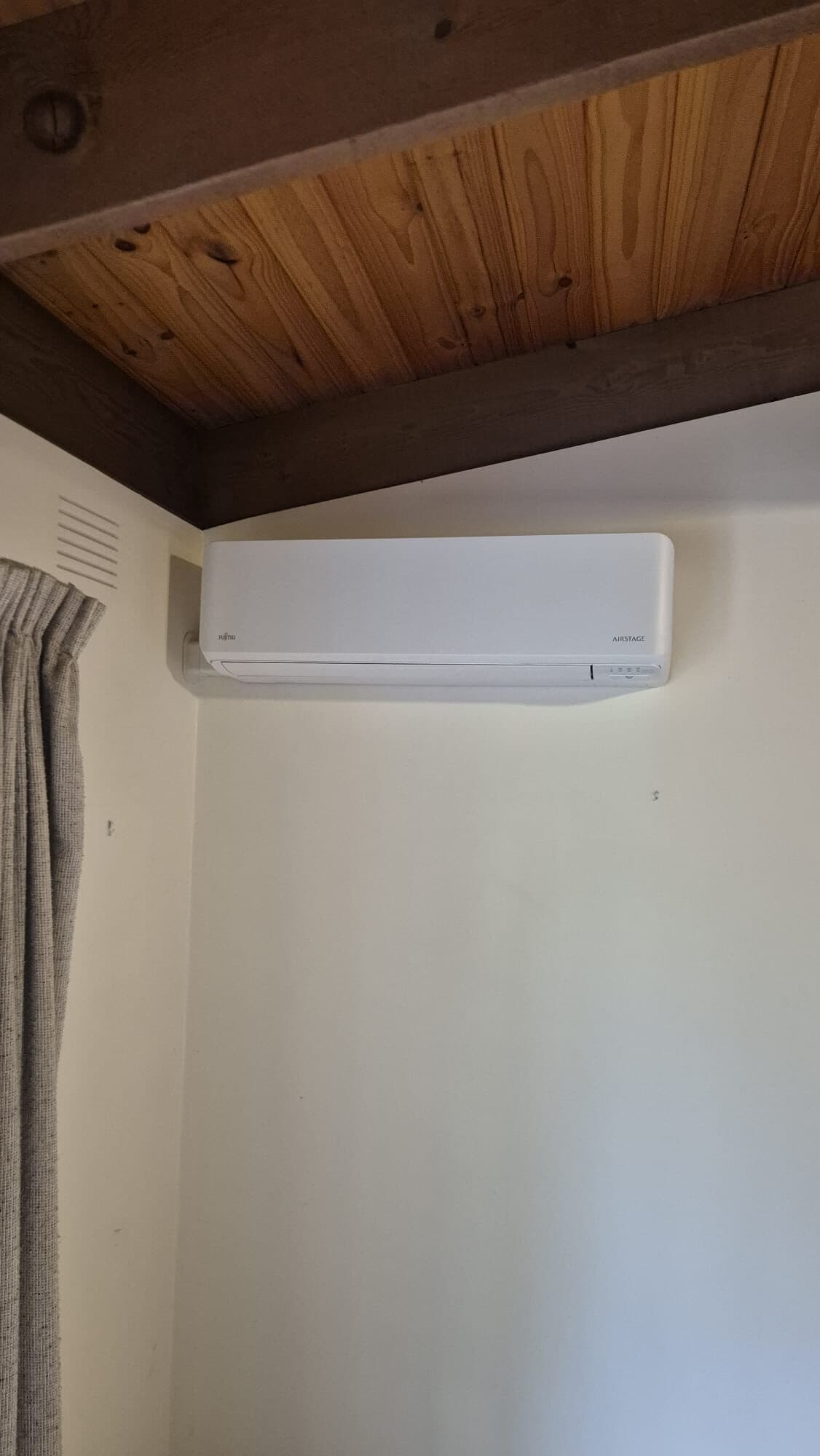 A wall-mounted split-system head cleanly installed where a white wall meets a raked timber-lined ceiling and exposed beam in Eltham