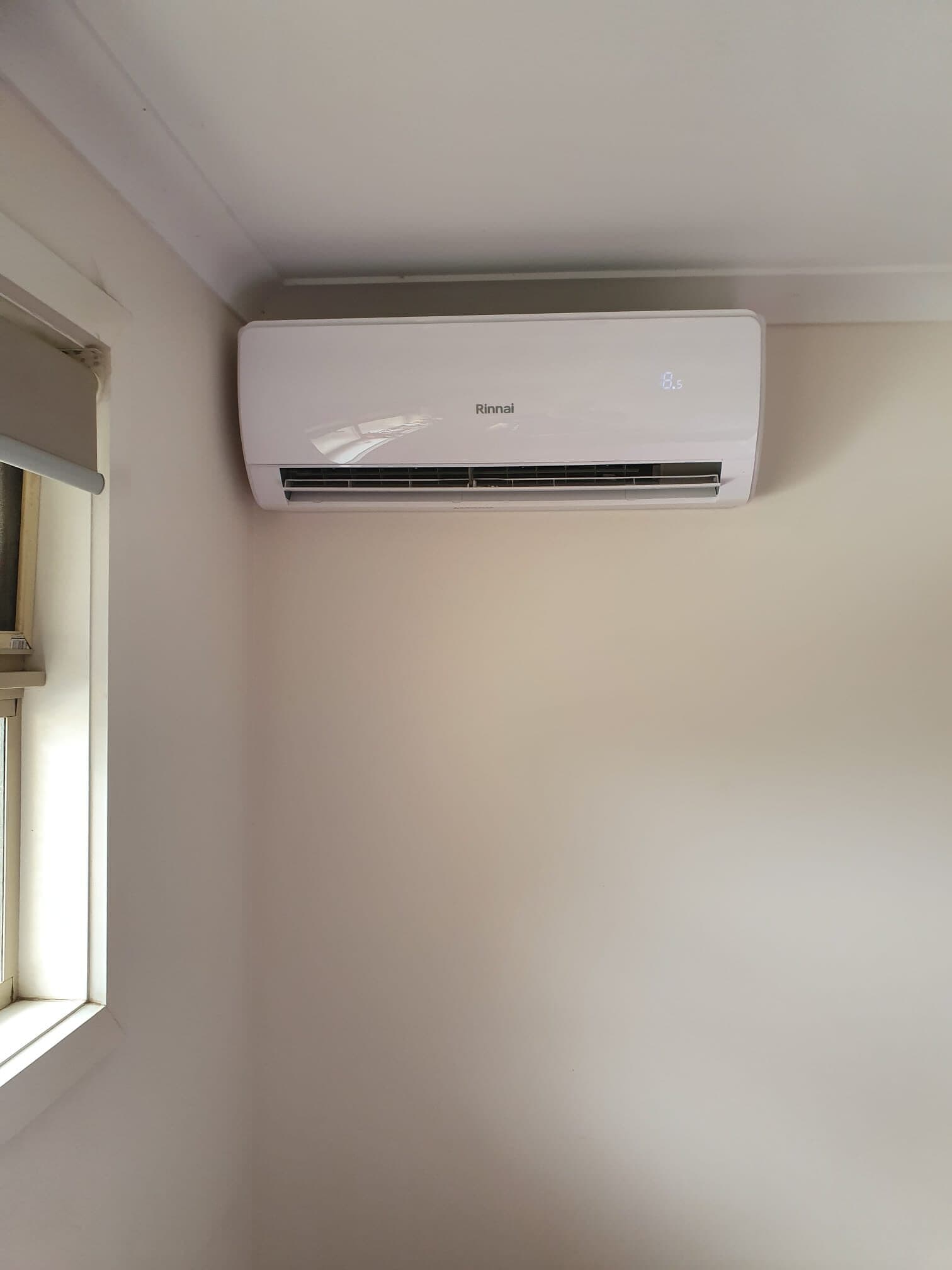 A bright wall-mounted split-system head in a corniced corner with window light in Glenroy