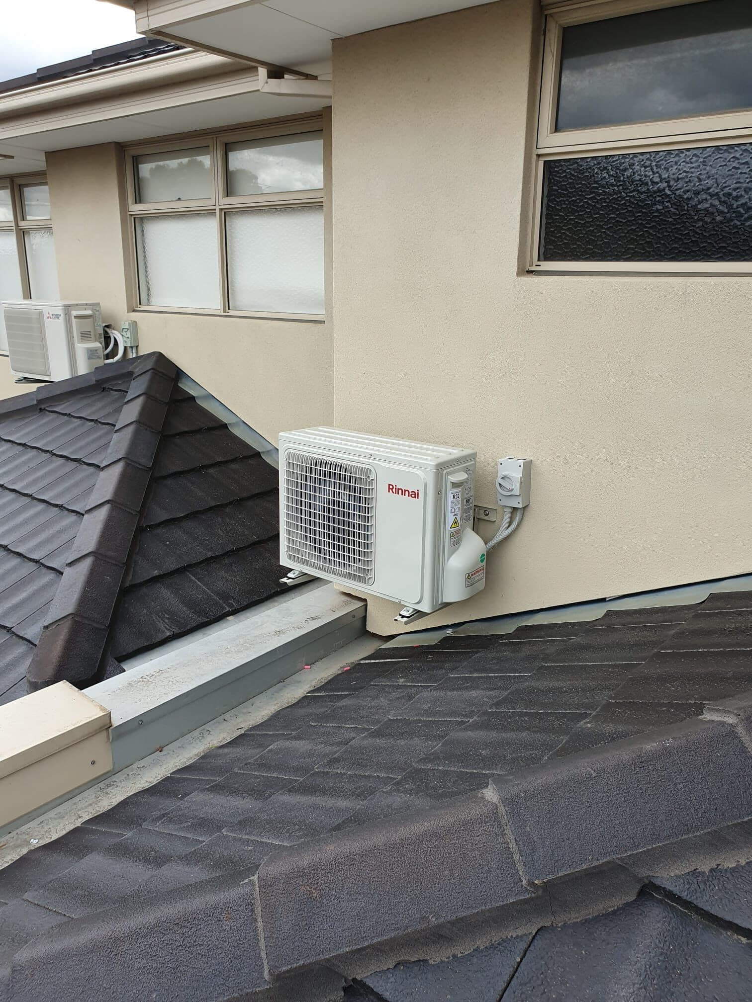 An outdoor condenser bracket-mounted on a render wall tucked between two pitched tile roofs in Glenroy with a neat lagged refrigerant line