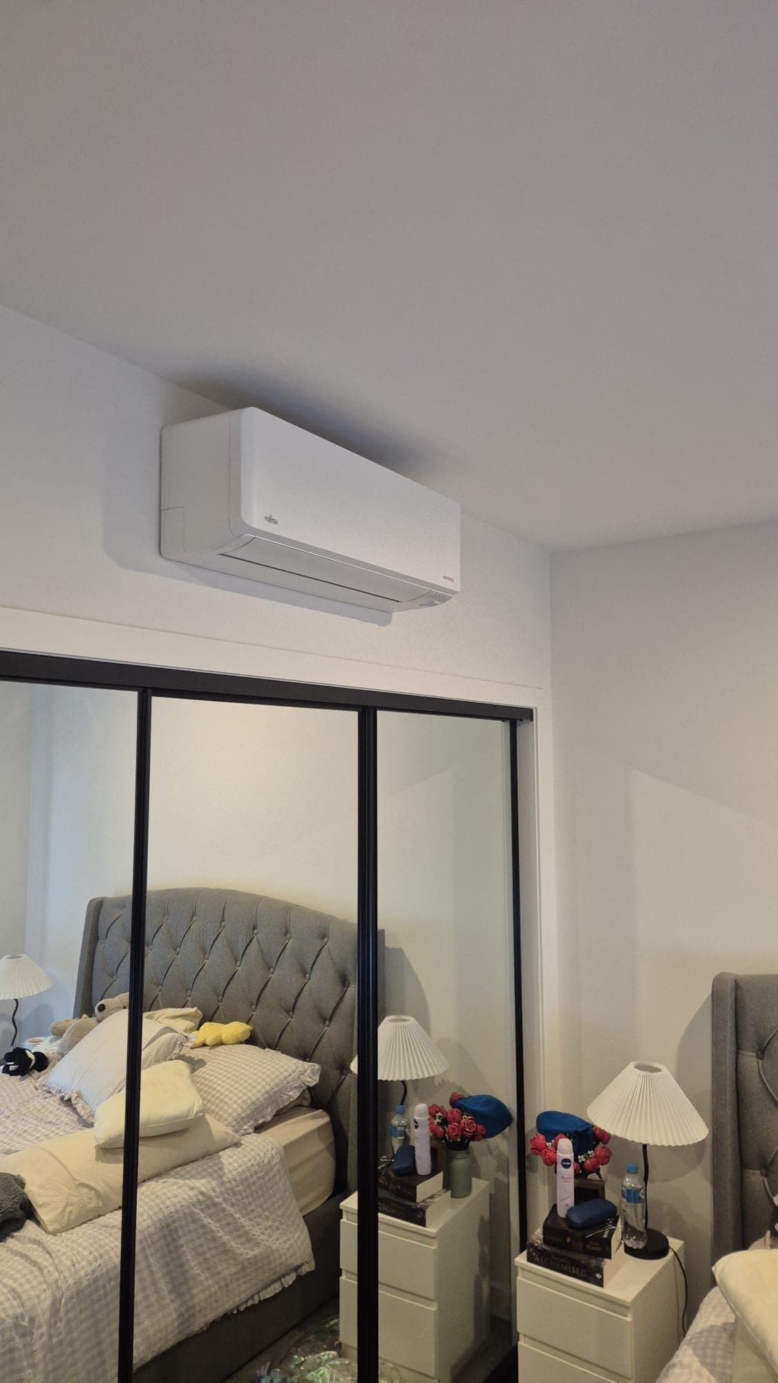 A wall-mounted split-system head installed neatly above a mirrored wardrobe in a bedroom in Mill Park