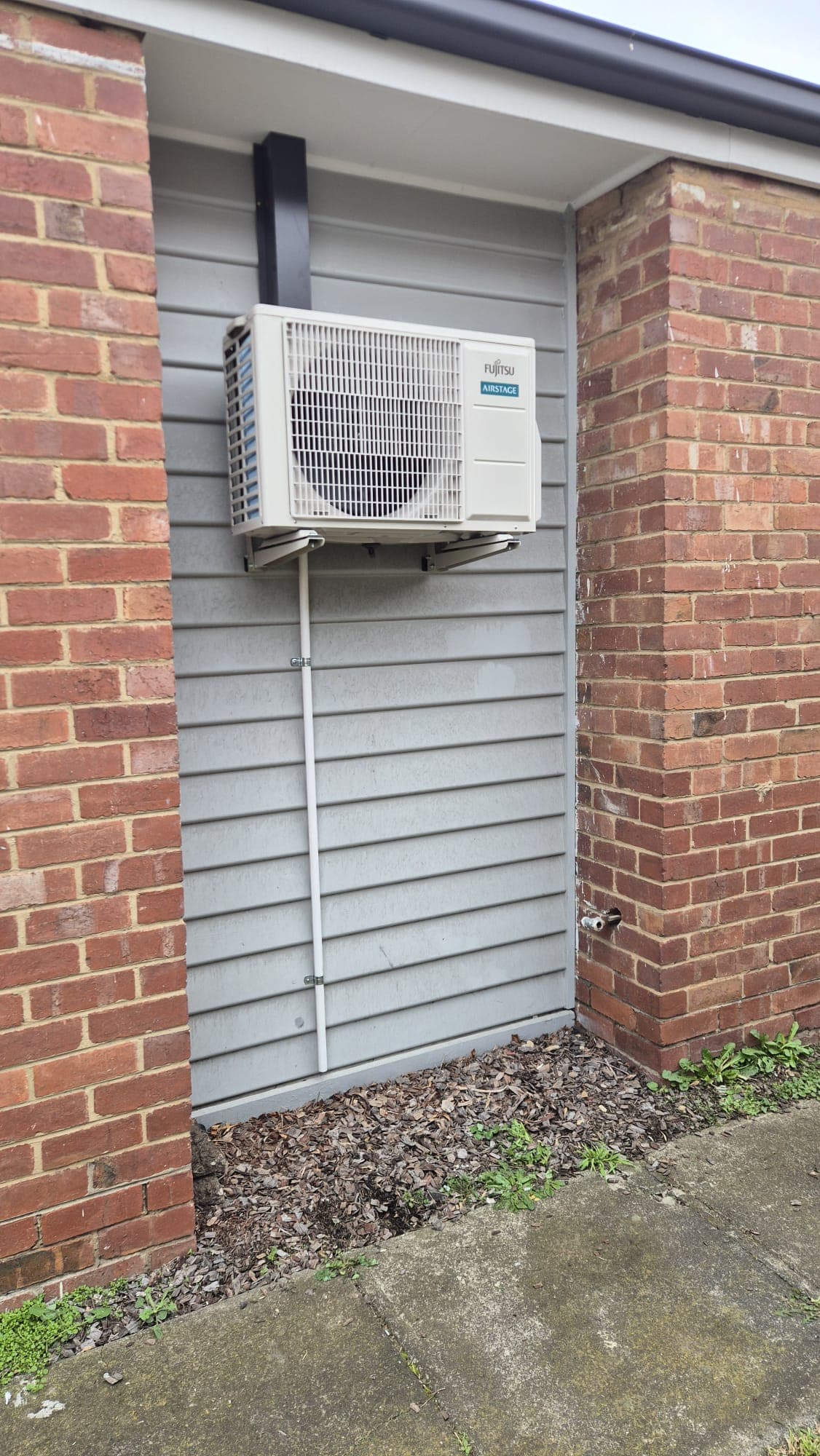 An outdoor condenser bracket-mounted on a weatherboard wall between two brick pillars in Pascoe Vale, with a neat conduit run to the slab