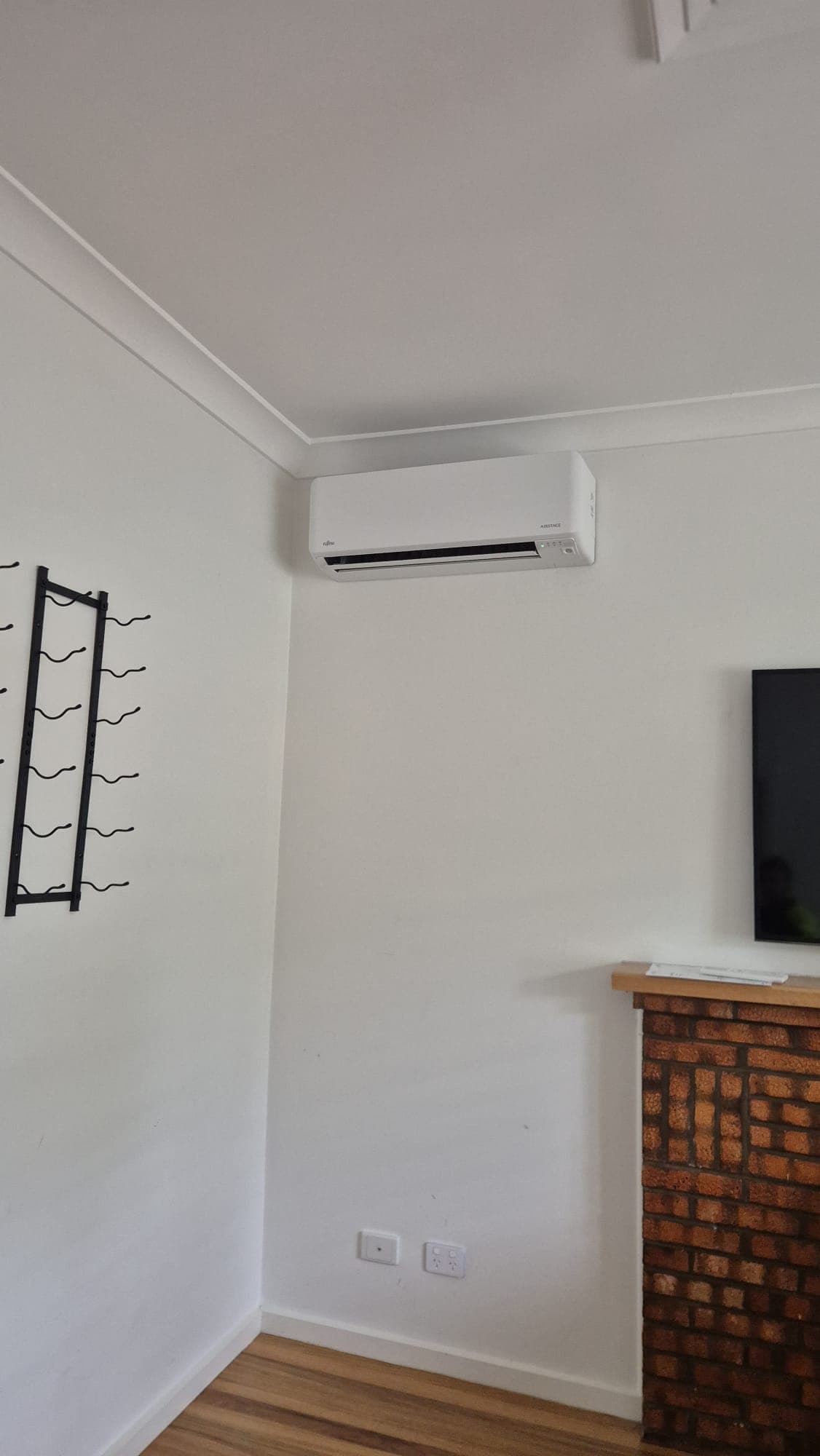 Wall-mounted split head high on a white wall beside a brick fireplace in a Pascoe Vale living room