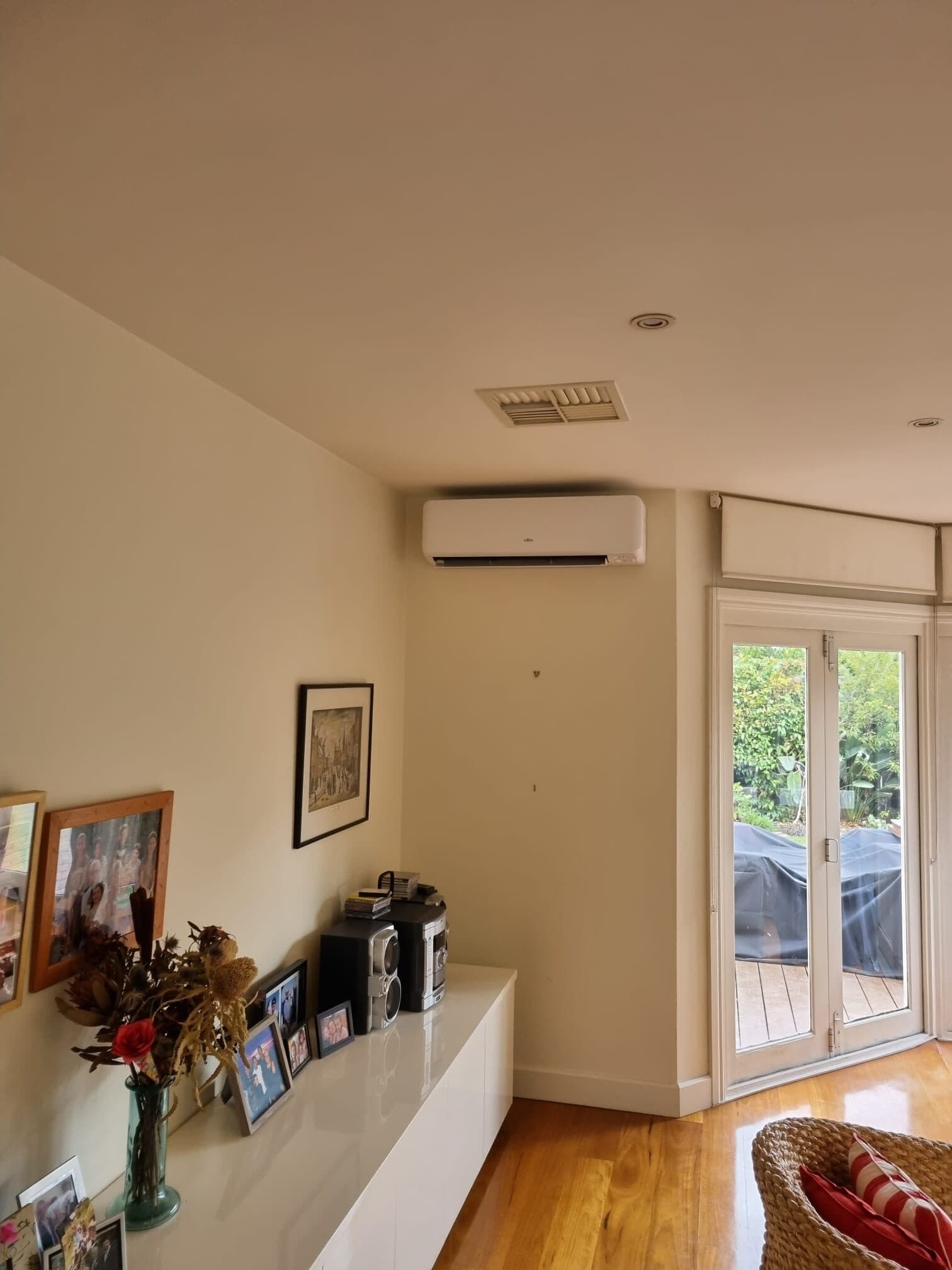 Wall-mounted split head high on the wall of a Werribee living room, with a sideboard and French doors onto a deck