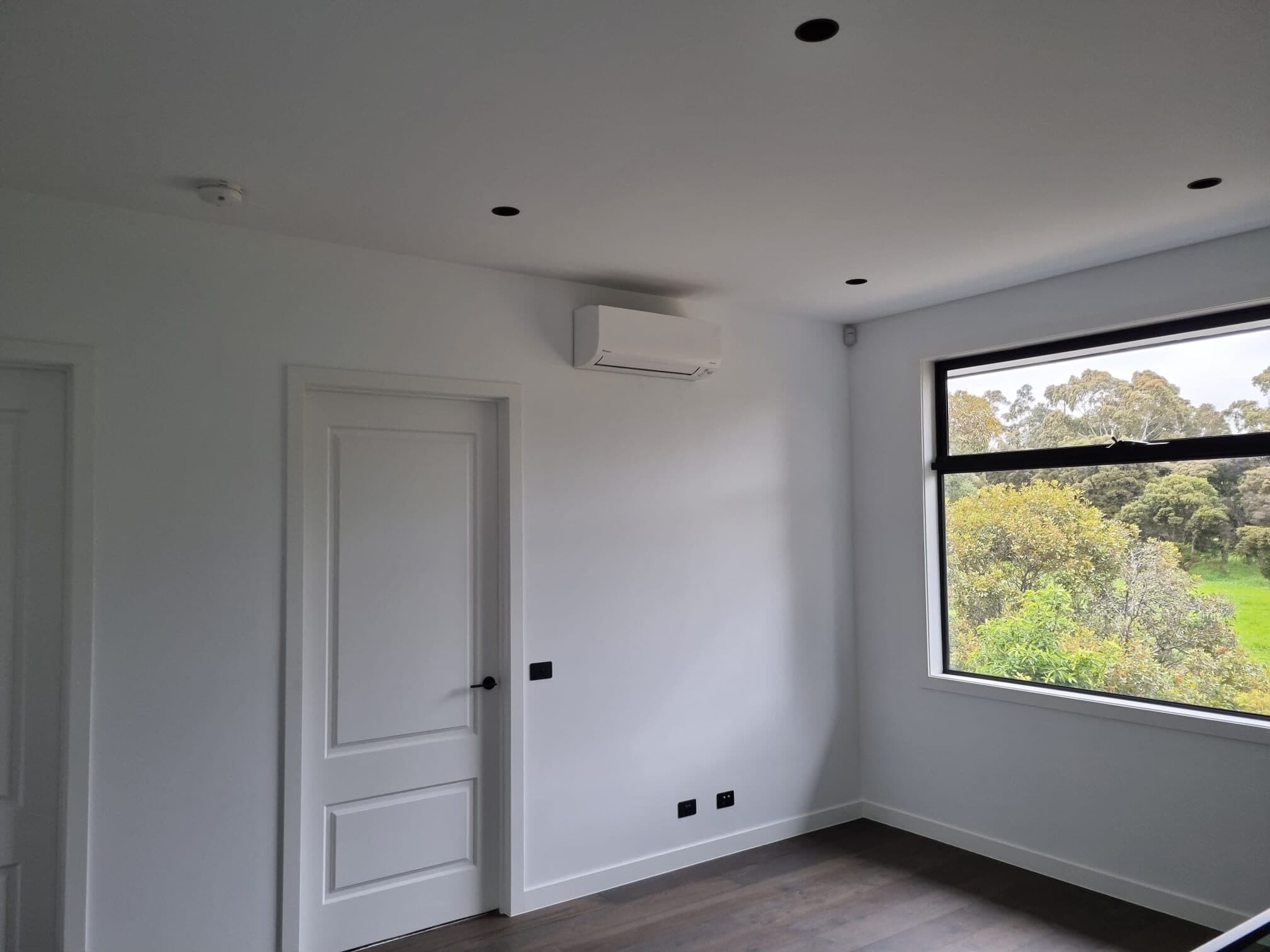 Wall-mounted split head beside a doorway in a finished room of a new Wheelers Hill home, with a window onto trees