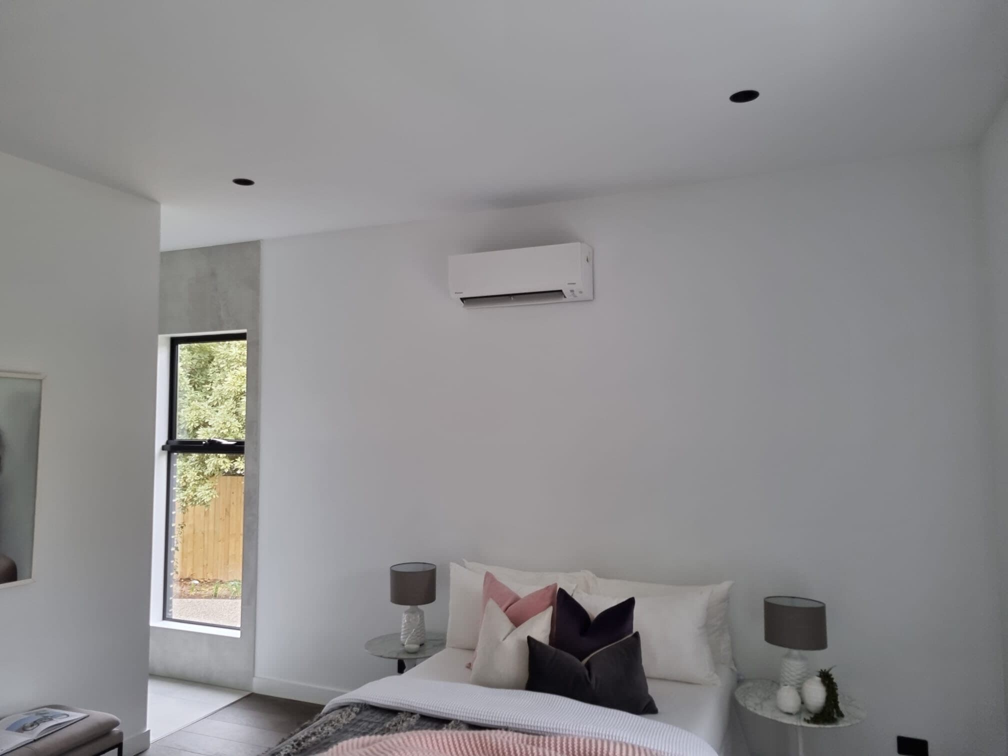 A wall-mounted split-system head above a dressed bed in a styled bedroom in Wheelers Hill