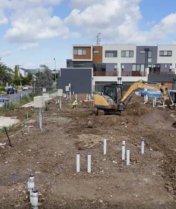Site works at Wattle House, screw-pile foundations and an excavator with completed townhomes behind