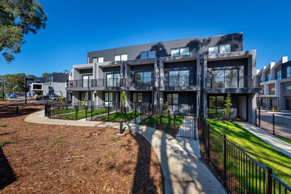 The Belmont Collection townhomes in Mill Park, a row of two-storey homes behind landscaped garden beds and a path