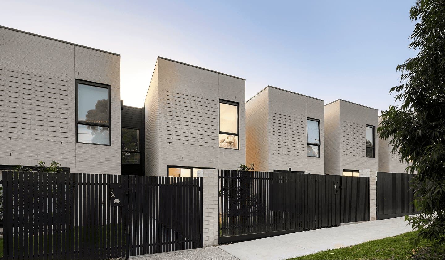 Early 3191 townhomes in Sandringham at dusk, a row of white-brick two-storey homes behind a dark steel fence